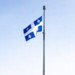 Quebec flag waving on a flagpole against a clear blue sky, symbolizing pride and identity.