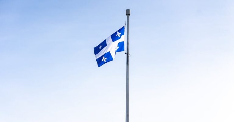 Quebec flag waving on a flagpole against a clear blue sky, symbolizing pride and identity.