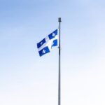 Quebec flag waving on a flagpole against a clear blue sky, symbolizing pride and identity.
