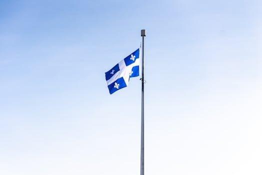 Quebec flag waving on a flagpole against a clear blue sky, symbolizing pride and identity.