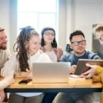 A diverse group of professionals engaged in a brainstorming session around a wooden table with technology present.